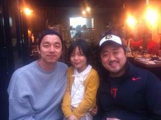 two men and a woman sitting at a table with food in front of them, smiling for the camera