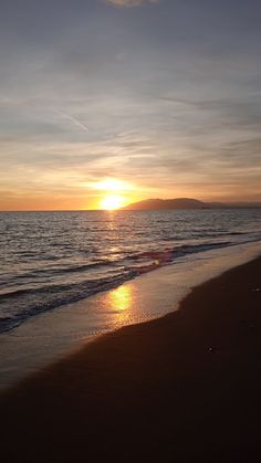 the sun is setting over the water at the beach with waves coming in to shore