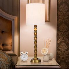 a gold lamp sitting on top of a table next to a white clock and flowers