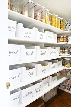 an organized pantry with white bins filled with food and labeled labels on the shelves