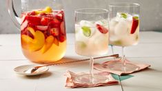 two glasses filled with fruit and ice on a table next to a pitcher full of water