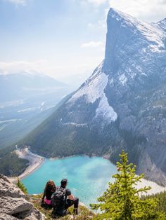 two people sitting on top of a mountain overlooking a lake