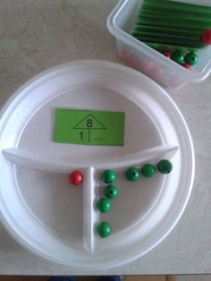 a plastic container filled with lots of green and red beads next to a white plate