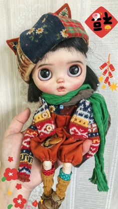 a hand holding a doll wearing a hat and scarf