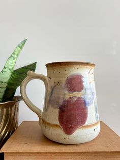 a coffee cup sitting on top of a wooden table next to a potted plant