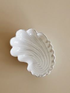 a white bowl sitting on top of a table next to a brown wall with a plant in it