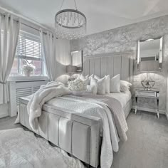 a large bed sitting in a bedroom next to a window covered in white blankets and pillows