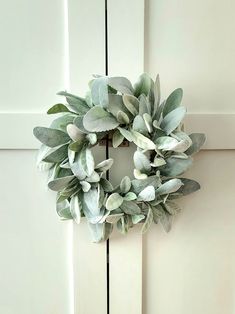 a wreath hanging on the side of a door with green leaves and greenery around it