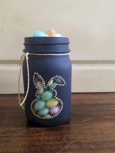 a jar filled with eggs and beads on top of a wooden table next to a wall