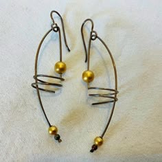 two metal hoops with gold balls hanging from them on a white cloth covered surface