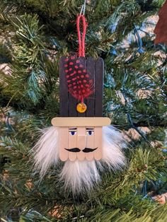 a wooden ornament hanging from a christmas tree with feathers and a mustache on it