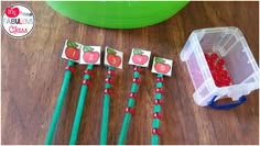 four apples and two green strawberries on top of a wooden table next to a plastic container