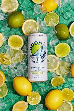 a can of soda surrounded by lemons and limes on green crushed paper with ice