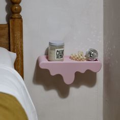 a pink shelf with a jar of cream on top of it next to a bed