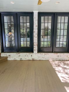 an empty room with wooden floors and black doors on both sides of the windows, in front of a white brick wall