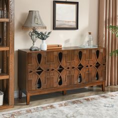 a wooden sideboard in a living room next to a lamp