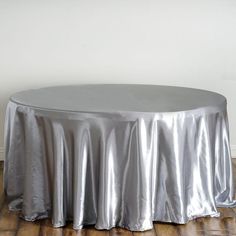 a round table covered in silver cloth on top of a hard wood floor next to a white wall