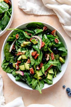 two white bowls filled with green salad on top of a table next to blueberries