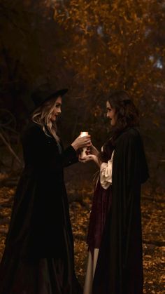 two women dressed as witches holding hands in the woods at night with trees and leaves behind them