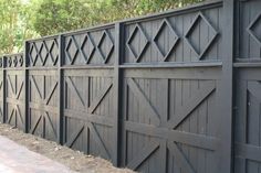 a black fence with wooden doors and windows on the side of it in front of some trees