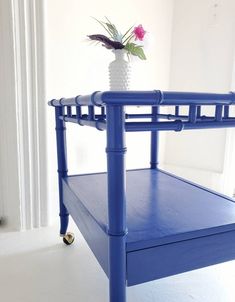 a blue table with a white vase on top and a flower in the bottom shelf