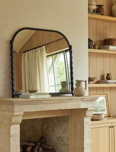 a fireplace in a living room with a mirror on the mantle and shelves behind it