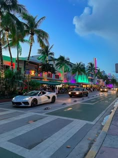 cars are driving down the street in front of buildings and palm trees at night time