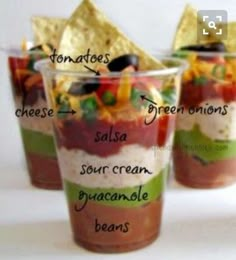 three cups filled with different types of food and chips on top of each cup are labeled