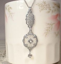 Offering an exquisite circa 1920s to 1930s era Edwardian/Art Deco filigree camphor glass crystal rhinestone pendant necklace. This one has such a gorgeous design! The rhodium plated  pendant features round thick frosted glass (camphor glass) with radial designs cut in the glass on the reverse side. The ornate filigree setting has such a beautiful detailed embossed design. The center is adorned with a diamond shaped piece that is pave set with a sparkly crystal rhinestone. I love the 1920s designed filigree work on this one!  The antique pendant hangs from a lacy very detailed filigree piece.  The filigree piece, in turn, hangs from a sterling silver chain that closes with a filigree tension hook clasp that is stamped "STERLING" on the back. Because I couldn't resist, I added a vintage pave Camphor Glass Jewelry, Camphor Glass Necklace, Wedding Something Old, Radial Design, Art Deco Filigree, Bridal Pendant, 1920s Vintage, Edwardian Art, 1930s Art