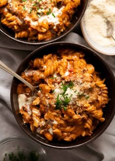 two black bowls filled with pasta and sauce on top of a white table cloth next to some bread