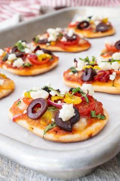 small flatbread pizzas with olives, tomatoes and cheese on a baking sheet