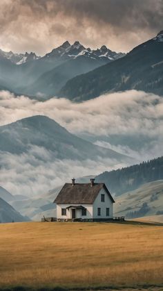 a house in the middle of a field with mountains in the background