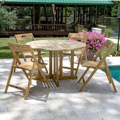 a wooden table and chairs next to a swimming pool with flowers in the foreground