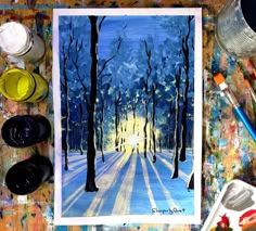 a painting on a table with paint and brushes next to it is an image of the sun shining through the trees