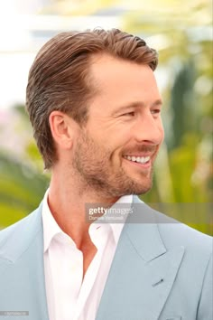 a close up of a person wearing a blue suit and white shirt with a smile on his face