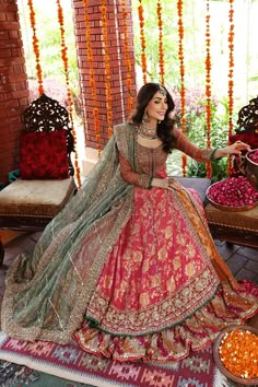 a woman in a red and green lehenga sitting on a rug with flowers