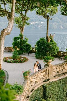 a bride and groom are sitting on a stone bridge overlooking the water at their wedding