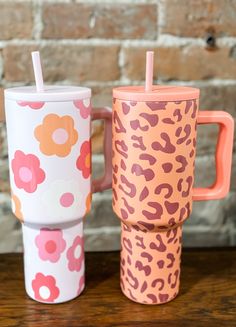 two colorful cups sitting next to each other on top of a wooden table in front of a brick wall