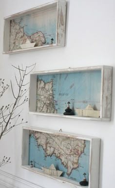 three framed maps hang on the wall above a mantel with a vase and branch