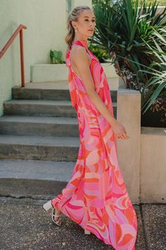 The Josephine Multicolor Printed Halter Maxi Dress is a vibrant and eye-catching garment that exudes summer elegance and playful charm. Its bold color palette of red-orange, pink, and purple creates a stunning visual impact, reminiscent of a tropical sunset or a vivid summer garden in full bloom. Crafted from lightweight fabric, this maxi dress flows effortlessly with every step, offering both comfort and style for warm-weather occasions. The halter neckline of the Josephine dress adds a touch of sophistication while providing support and structure to the silhouette. Its sleeveless design allows for freedom of movement, making it perfect for outdoor events or beachside strolls. A geometric pattern adorns the fabric of the dress, adding depth and visual interest to the overall design. The p Playful Pink V-neck Dress, Pink Sleeveless Maxi Dress Beach Cover-up, Orange Sleeveless Dress For Summer Parties, Playful Orange Sleeveless Dress, Spring Poolside Maxi Dress, Vibrant Print Halter Neck Dress For Spring, Pink Sleeveless Beach Dress For Spring, Spring Halter Neck Dress With Vibrant Print, Pink Sleeveless Beach Dress For Party