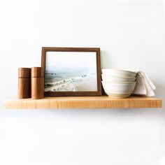 a wooden shelf with a bowl and two cups on it next to a framed photograph