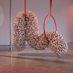 a sculpture made out of white balls hanging from red ropes in front of a wall