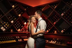 a man and woman standing next to each other in front of wine bottles