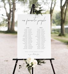 a seating sign with flowers on it and greenery around the table for an outdoor ceremony