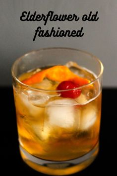 a glass filled with ice and fruit on top of a black table next to a sign that reads elderflower old fashioned