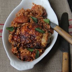 a white bowl filled with meat and rice on top of a table next to a knife