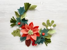 felt christmas wreath with poinsettis and pine cones on white wooden background, top view