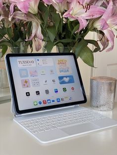 a laptop computer sitting on top of a desk next to a vase filled with flowers