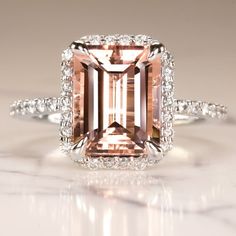 an engagement ring with a large pink diamond surrounded by white diamonds on a marble surface