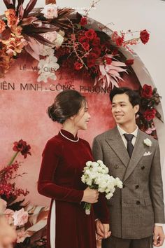 a man and woman standing next to each other in front of a wall with flowers